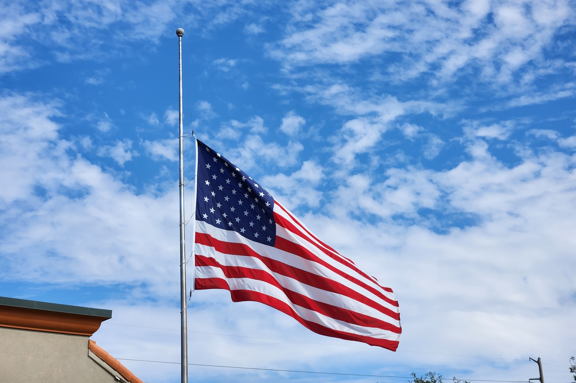 USA national flag waving lowered to half mast on wind against blue sky.